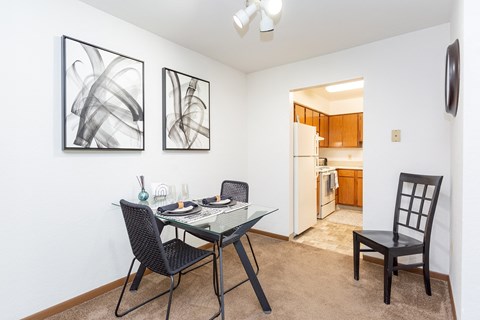 a dining area with a glass table and chairs and a kitchen in the background